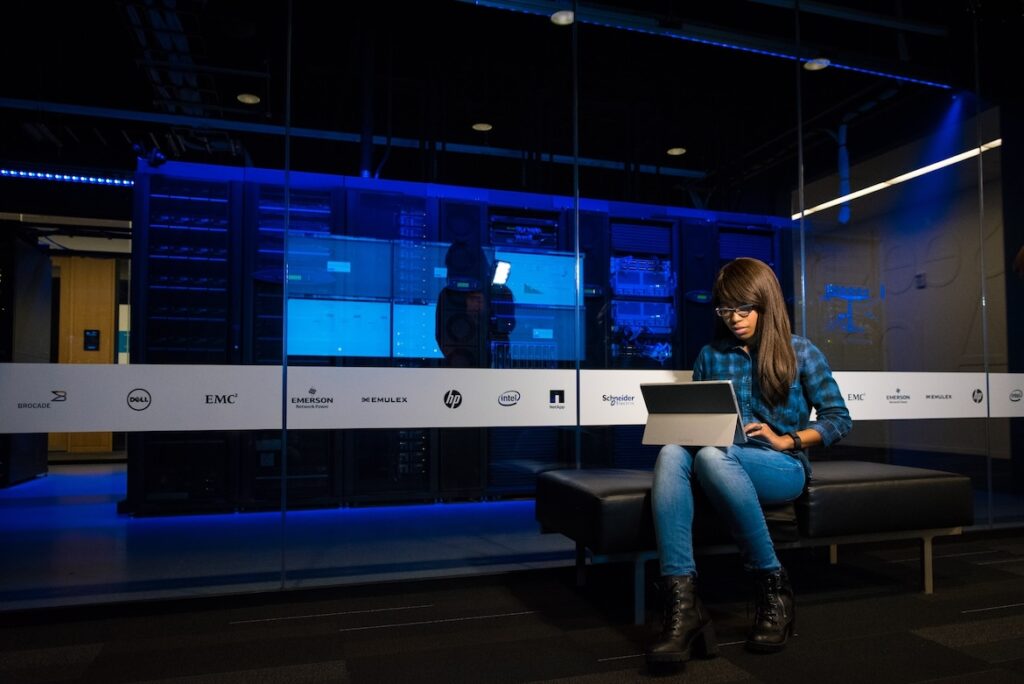 An engineer at her laptop beside a server rack, tracing a failure through root-cause analysis.